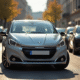 Voiture Peugeot 208 argentée sur une rue urbaine ensoleillée
